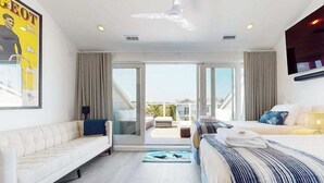 Ein modernes Hotelzimmer mit Sofa, Bett, Deckenventilator und Blick durch eine Glastür ins Freie.