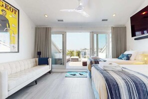 A modern hotel room with a sofa, a bed, a ceiling fan, and a view through a glass door to the outside. - Town of Dewey Beach- Inviting newly renovated townhouse with ocean views (Dewey Beach)