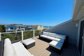 A balcony with a white sofa, a small table, and a wicker ottoman. - Town of Dewey Beach- Inviting newly renovated townhouse with ocean views (Dewey Beach)