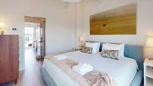 Ein Hotelzimmer mit einem großen Bett, einem Deckenventilator, einem Gemälde an der Wand und Blick durch eine geöffnete Tür.