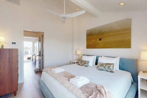 A hotel room with a large bed, a ceiling fan, a painting on the wall, and a view through an open door. - Town of Dewey Beach- Inviting newly renovated townhouse with ocean views (Dewey Beach)