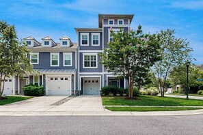 A multi-story residential building with a garage, a driveway, and well-maintained landscaping. - Sawgrass at White Oak Creek - townhome with AC, pools & gyms (Rehoboth Beach)
