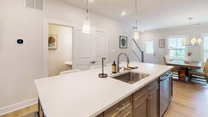 Una cocina moderna con una isla central, iluminación colgante y una zona de comedor con una escalera.