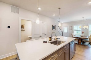 A modern kitchen with a central island, pendant lighting, and a dining area with a staircase. - The Peninsula spacious home w/community pool, hot tub, tennis courts (Millsboro)