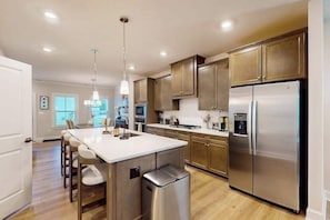 A modern kitchen with a central island, stainless steel appliances, and wooden cabinets. - The Peninsula spacious home w/community pool, hot tub, tennis courts (Millsboro)