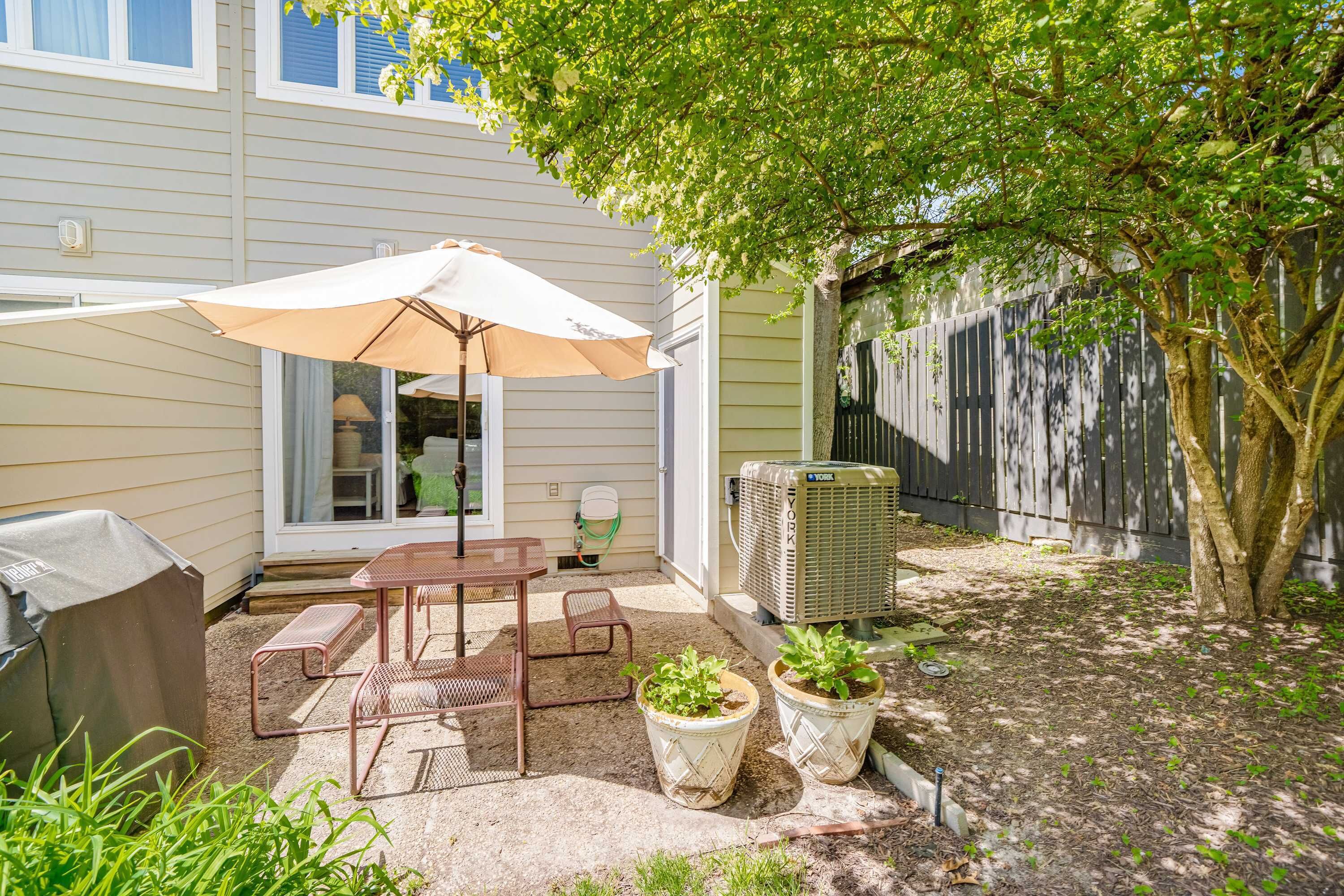 Une terrasse avec une table et des chaises, un barbecue abrité et des plantes en pot.