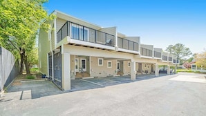 Un immeuble résidentiel à plusieurs étages, doté de balcons, d’un espace de stationnement couvert et offrant une vue sur un ciel dégagé.
