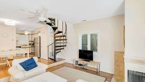 Un salon moderne avec un canapé blanc, une table basse, un téléviseur, une cheminée et un escalier en colimaçon.