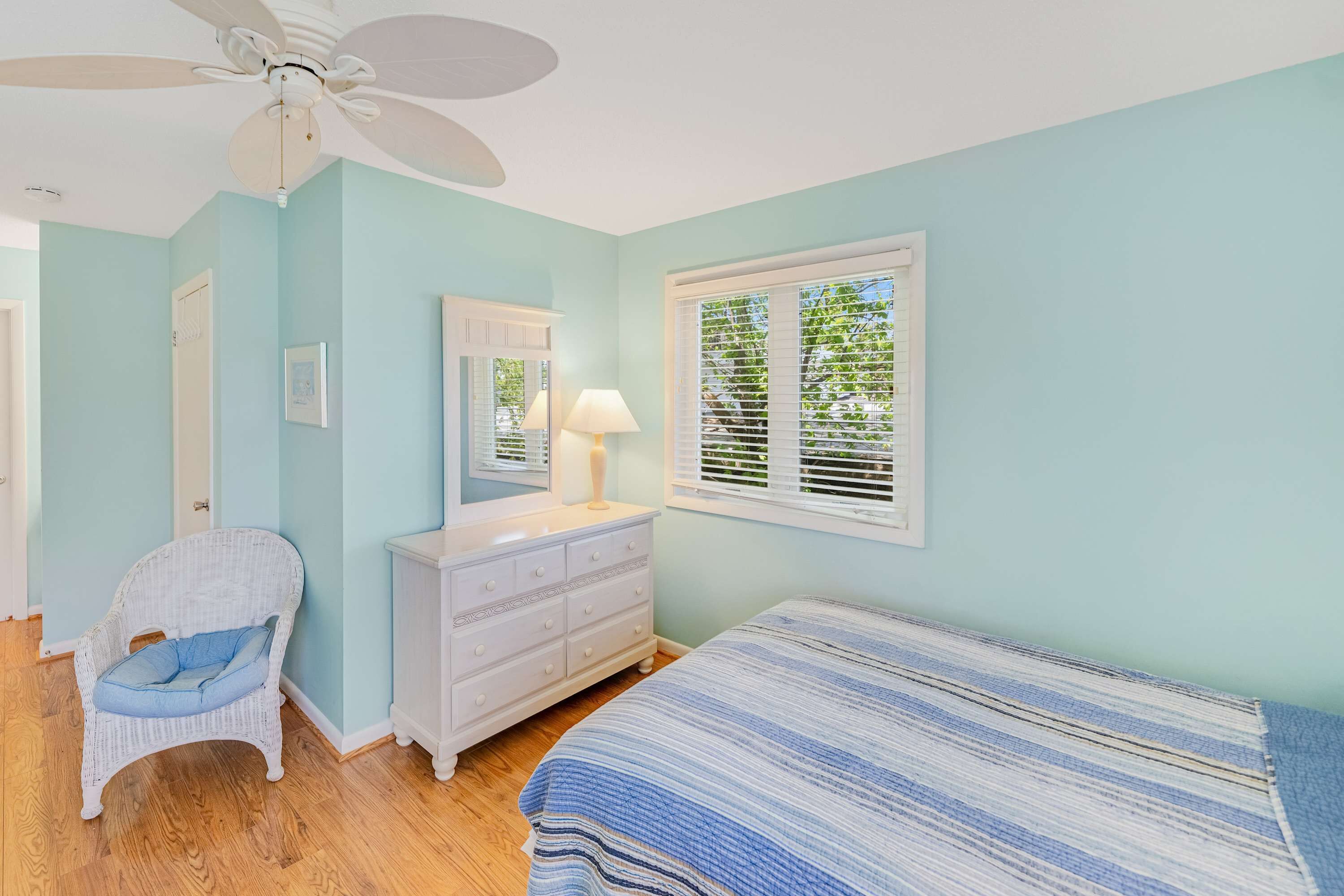 A bedroom with a bed, a chair, a dresser, a ceiling fan, and a window with blinds.