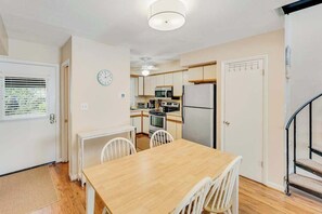 A compact kitchen with a dining table, chairs, a clock, and a staircase. - Lovely dog-friendly Scarborough Village home with spiral staircase, patio & W/D (Rehoboth Beach)