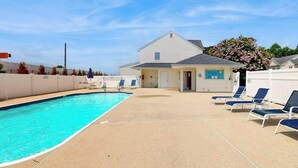 A swimming pool with lounge chairs, a small building with a garage, and a tree with pink flowers. - Taramino Spacious Townhouse w/shared pool, W/D & free WIFI (Lewes)