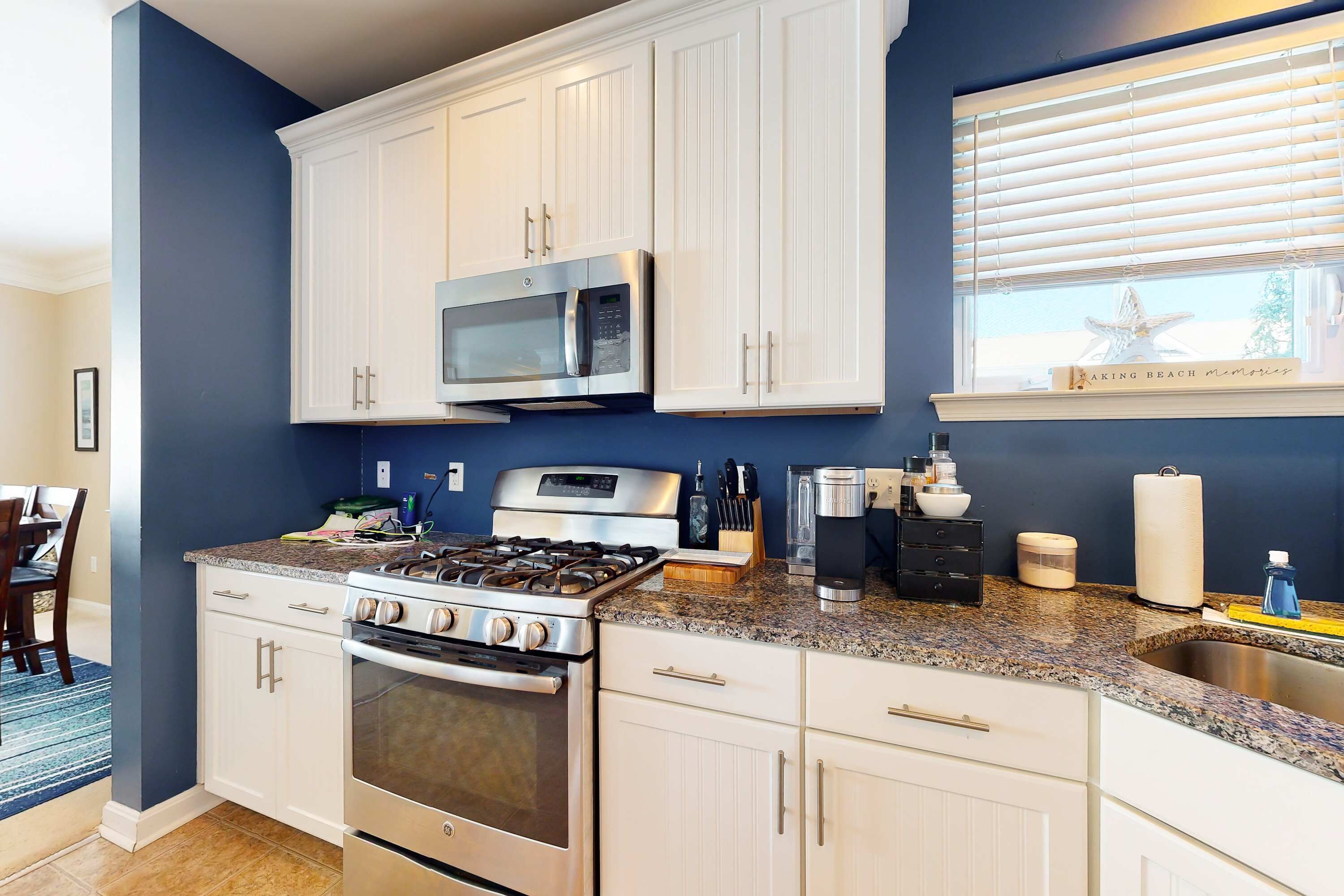 A kitchen with white cabinets, a stainless steel stove, a microwave, and a window with blinds.