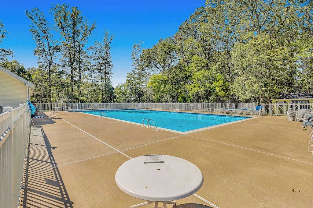 Una piscina con cubierta blanca, rodeada de árboles y una zona vallada.