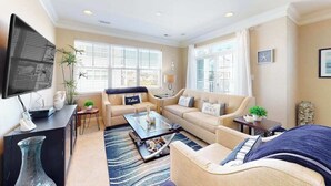 A living room with a sofa, coffee table, TV, and windows with blinds. - Grande at Canal Pointe condo with pools, tennis, gym, & private balcony (Rehoboth Beach)