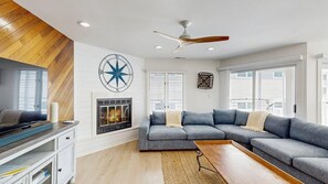 A modern living room with a sectional sofa, a fireplace, a ceiling fan, and a large wall clock. - Town of Dewey Beach condo w/deck, balcony, walk to beach, close to restaurants (Dewey Beach)