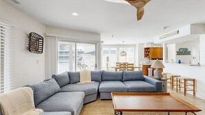 A modern living room with a sectional sofa, a wooden coffee table, and a dining area with a table and chairs. - Town of Dewey Beach condo w/deck, balcony, walk to beach, close to restaurants (Dewey Beach)