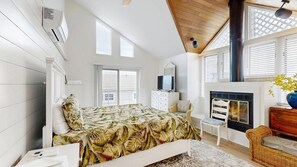 Un dormitorio con cama, cómoda, silla, chimenea y ventanas amplias.