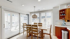 A dining area with a table and chairs, a hanging light fixture, and a view through large windows. - Town of Dewey Beach condo w/deck, balcony, walk to beach, close to restaurants (Dewey Beach)