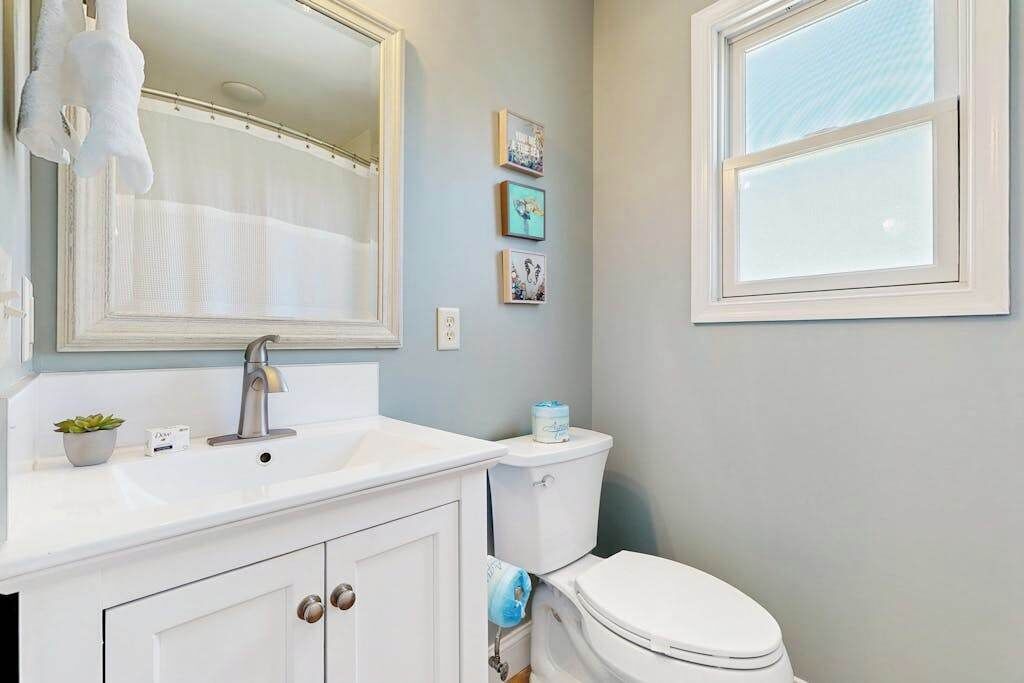 A bathroom with a white sink, a mirror, a toilet, and a window.