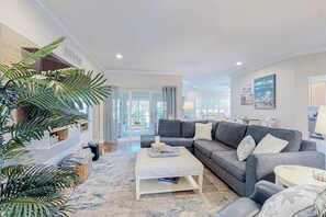 Ein Wohnzimmer mit grauem Sofa, Hocker mit Streifenmuster und einer großen Pflanze.