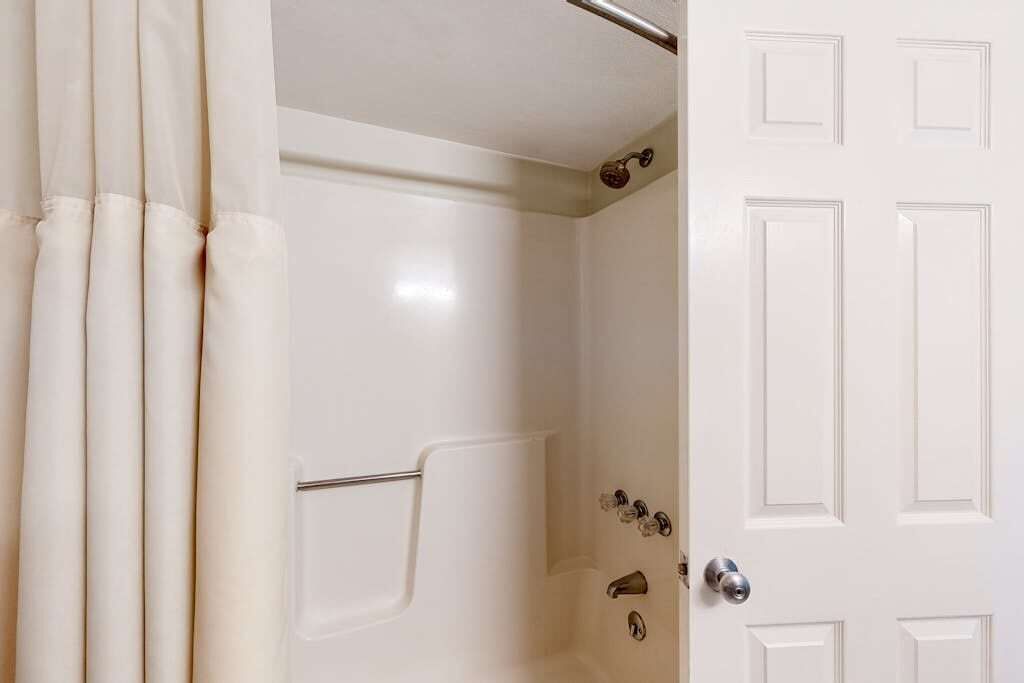 Une salle de bain avec un rideau de douche, une baignoire et une porte dotée d’une poignée.