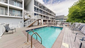 A pool area with a wooden deck, a pool, and a building with multiple balconies. - Town of Rehoboth Beach, Wilmington Ave #317 | Condo in Rehoboth Beach (Rehoboth Beach)