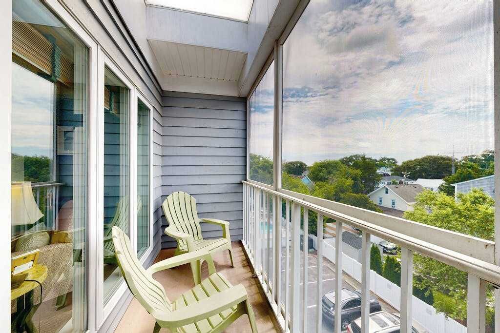 Ein Balkon mit zwei Adirondack-Stühlen, einer Glastür und Blick auf eine Wohngegend.