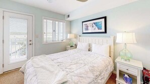 A bedroom with a bed, a ceiling fan, a window with blinds, a bedside table with a lamp, and a framed picture on the wall. - Town of Rehoboth Beach, Wilmington Ave #317 | Condo in Rehoboth Beach (Rehoboth Beach)