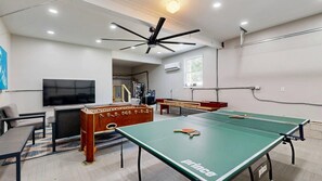 Ein Zimmer mit Tischtennisplatte, Kicker, Flachbildfernseher und Deckenventilator.