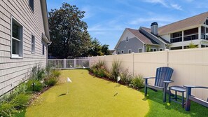 Ein Garten mit Kunstgrashalm, einem weißen Zaun und einem blauen Stuhl.
