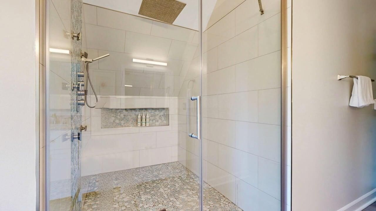 A glass-enclosed shower with a tiled floor, a white towel hanging on the wall, and a tiled wall with a rectangular window.
