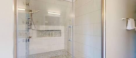 A glass-enclosed shower with a tiled floor, a white towel hanging on the wall, and a tiled wall with a rectangular window.