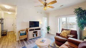 Un salon doté d’un ventilateur de plafond, d’un téléviseur, d’un canapé, d’une table basse et d’une grande fenêtre.