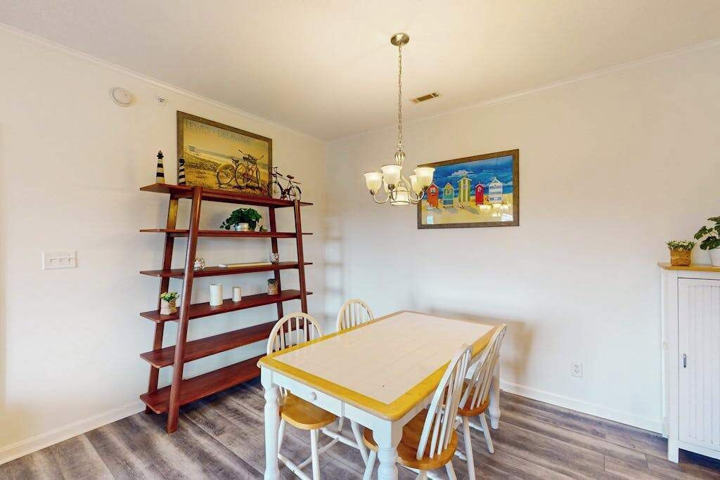 Uma sala de jantar com uma mesa e cadeiras de madeira, uma estante e duas pinturas penduradas na parede.