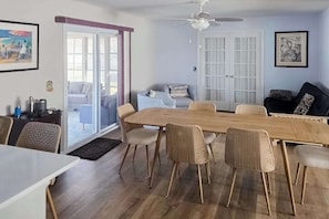 A dining area with a wooden table and wicker chairs, a ceiling fan, and a sliding glass door leading to an outdoor seating area. - Rehoboth Beach home near beach & boardwalk with grill, streaming, & W/D (Rehoboth Beach)