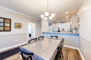 A dining area with a large table, chairs, a chandelier, and a kitchen area in the background. - Stunning Condo- Pool and Hot Tub- Convenient Beach Access! (Rehoboth Beach)