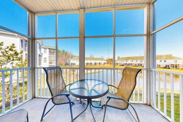 A covered outdoor area with a table and chairs, large windows, and a view of buildings and a body of water. - Stunning Condo- Pool and Hot Tub- Convenient Beach Access! (Rehoboth Beach)