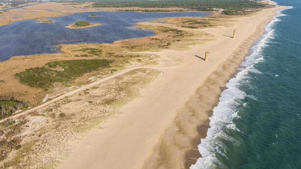 Vue aérienne d’une zone côtière avec une plage de sable, des étendues d’eau et une végétation clairsemée.