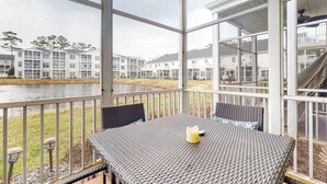 Un espace extérieur abrité, doté d’une table et de chaises, offrant une vue sur un plan d’eau et avec un bâtiment en arrière-plan.