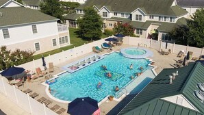 Une piscine entourée de chaises longues et de parasols, elle-même délimitée par une clôture, avec des maisons en arrière-plan.