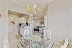 A dining area with a glass table, white chairs, and a chandelier.