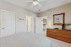 Une chambre à coucher avec un lit, une commode, un ventilateur de plafond et un miroir.