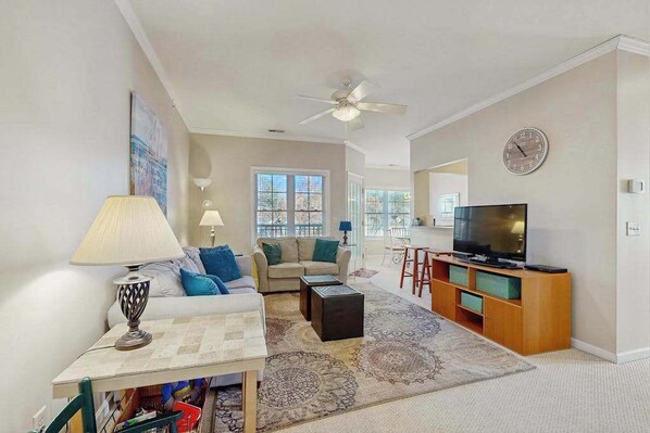 A living room with a sofa, coffee table, TV stand, and a ceiling fan.