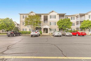 A multi-story apartment building with a central entrance, parking lot, and trees.