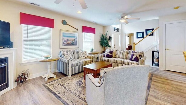 A living room with a fireplace, striped sofas, a coffee table, and ceiling fans. - The Palms condo near the beach with on-site pool & enclosed patio (Rehoboth Beach)
