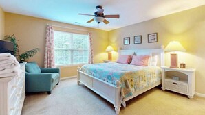 A bedroom with a bed, a chair, a nightstand, a ceiling fan, and a window. - The Palms condo near the beach with on-site pool & enclosed patio (Rehoboth Beach)