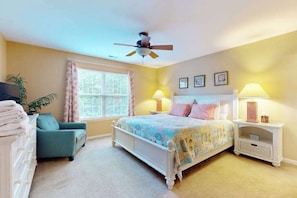 A bedroom with a bed, a chair, a nightstand, a ceiling fan, and a window. - The Palms condo near the beach with on-site pool & enclosed patio (Rehoboth Beach)
