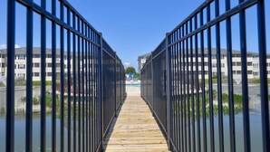 A wooden pathway flanked by metal railings leading to a building with a swimming pool. - The Palms condo near the beach with on-site pool & enclosed patio (Rehoboth Beach)