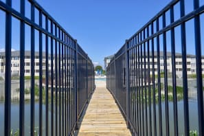 A wooden pathway flanked by metal railings leading to a building with a swimming pool. - The Palms condo near the beach with on-site pool & enclosed patio (Rehoboth Beach)