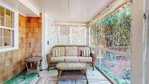 Ein überdachter Balkon mit einem Korbssessel, einem kleinen runden Tisch und einem gemusterten Teppich.
